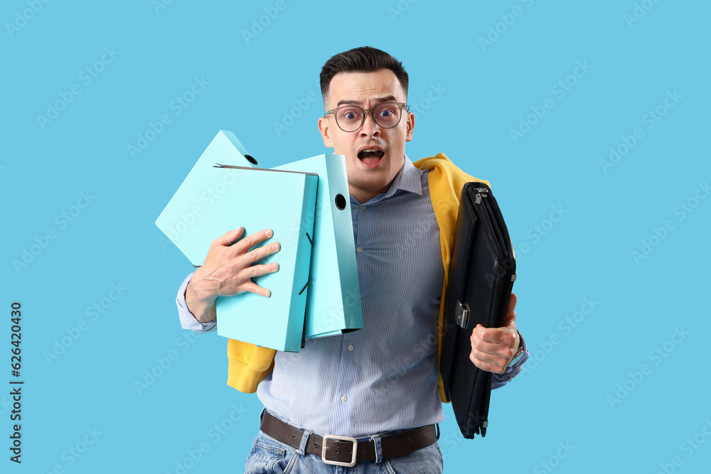 Stressed businessman with folders and briefcase on blue background. Deadline concept