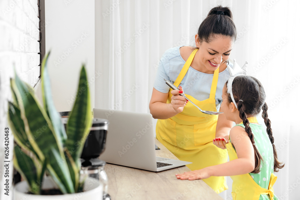 Working mother with her little daughter cooking in kitchen