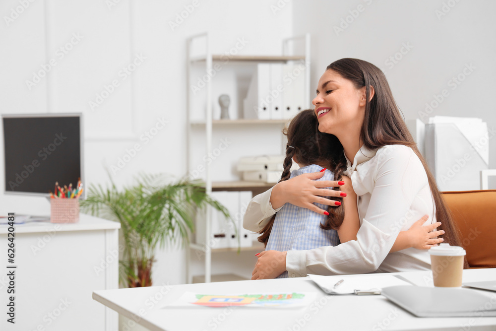 Working mother with her little daughter hugging in office