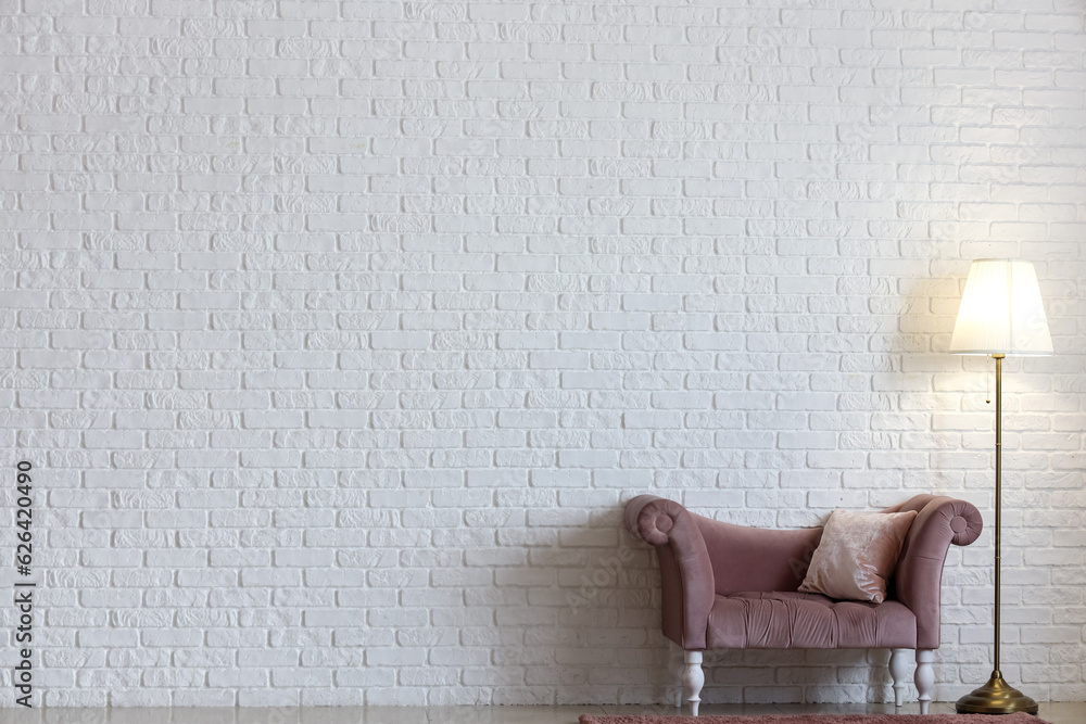 Glowing lamp with armchair near white brick wall in room