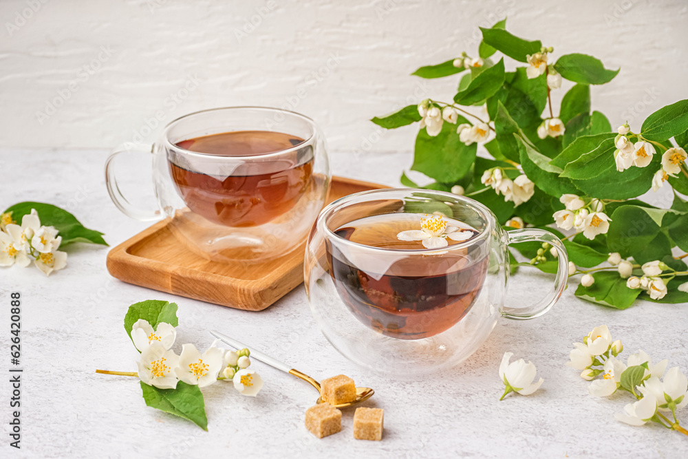 Glass cups of tea, sugar and beautiful jasmine flowers on light background