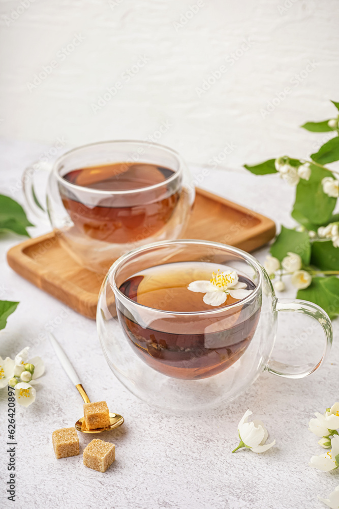 Glass cups of tea, sugar and beautiful jasmine flowers on light background