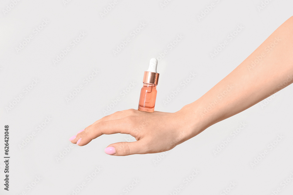 Hand of woman with bottle of cosmetic oil on light background