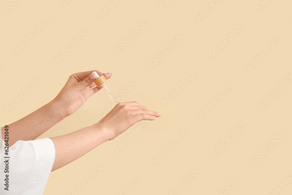 Hands of woman with cosmetic oil on beige background