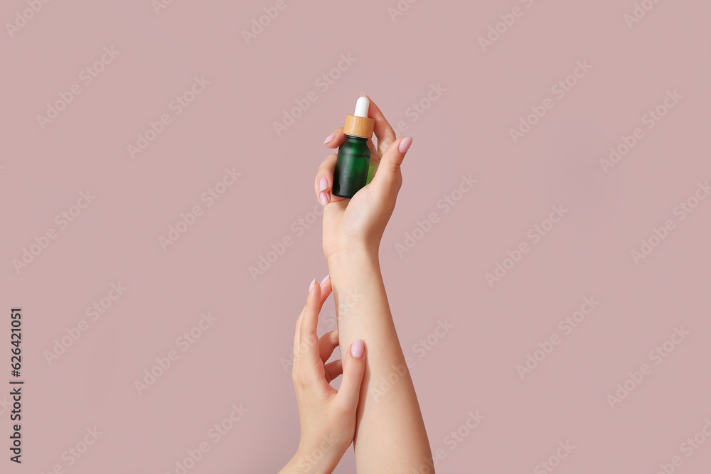 Hands of woman with bottle of cosmetic oil on pink background