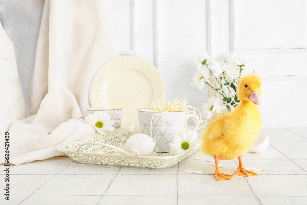 Cute duckling, tray with cups and chamomile flowers on white tile table