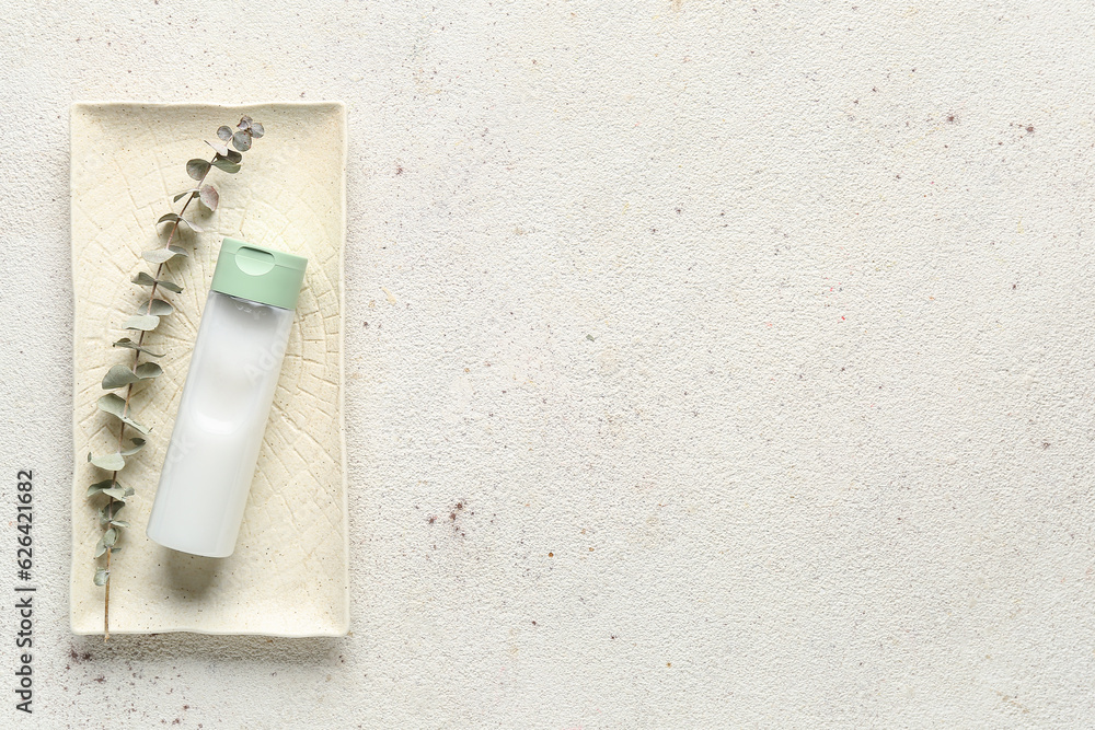 Plate with bottle of cosmetic product and eucalyptus branch on light background