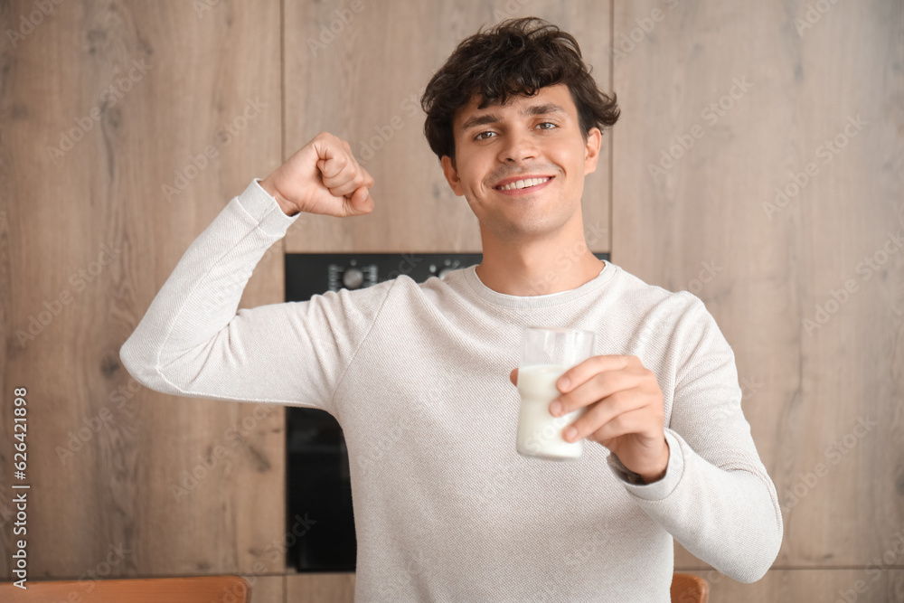 Strong young man with glass of milk in kitchen