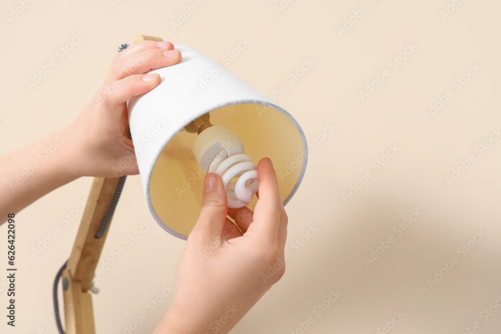 Woman changing light bulb in lamp on beige background, closeup