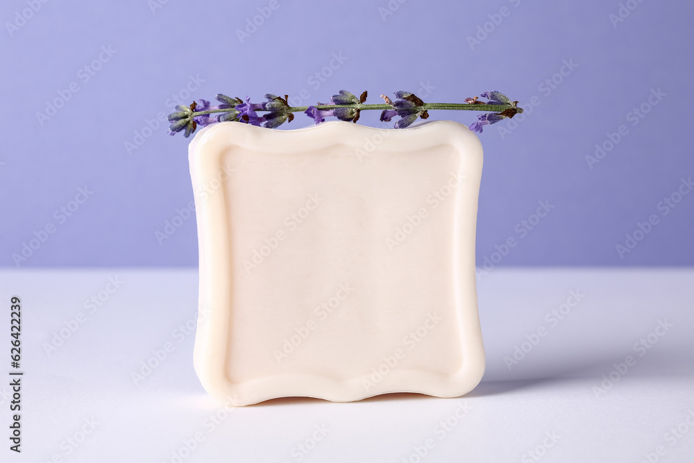 Soap bar with lavender flower on light table against color background