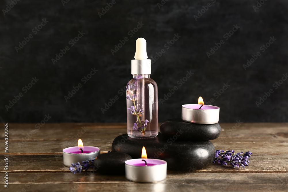 Bottle of essential oil, spa stones and burning candles on wooden table