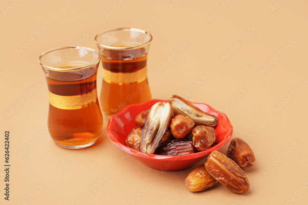 Bowl with dried dates and glasses of Turkish tea on brown background