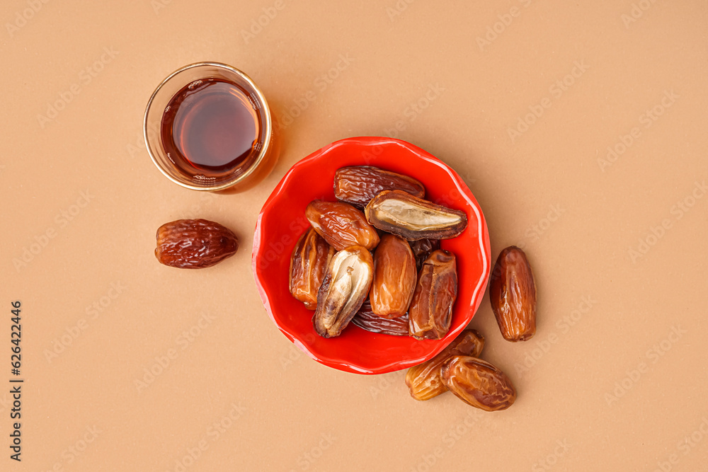 Bowl with dried dates and glass of Turkish tea on brown background