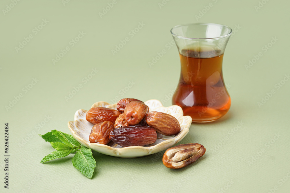 Plate with dried dates and glass of Turkish tea on green background