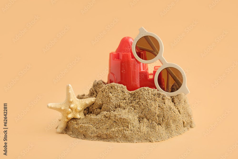 Castle made of sand with beach toy, starfish and sunglasses on orange background