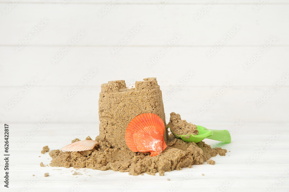 Castle made of sand with seashells and shovel on white wooden background