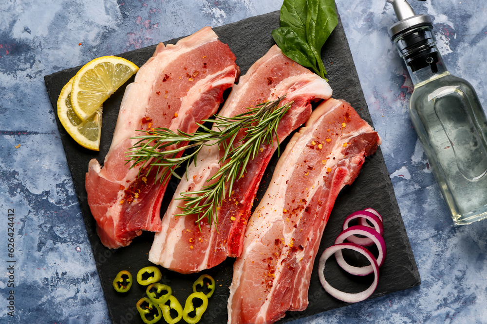 Slate board with raw pork ribs with spices and oil on color background, closeup