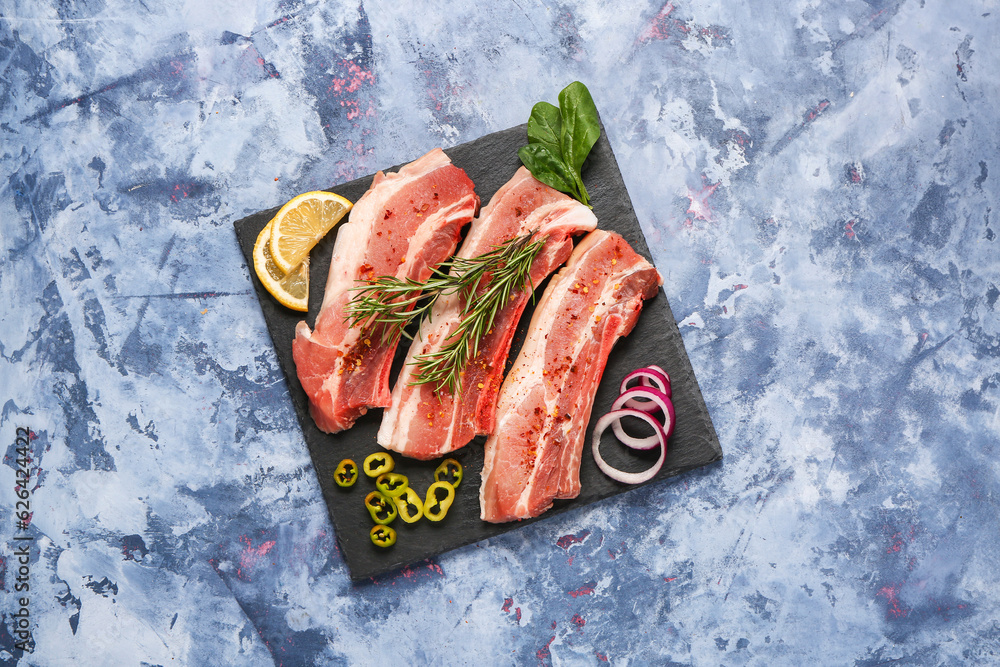 Slate board with raw pork ribs with spices on color background