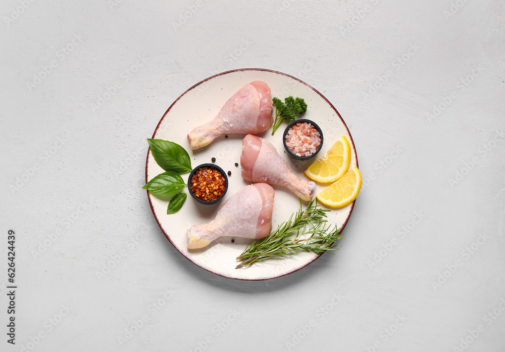 Plate with raw chicken legs, spices and herbs on light background