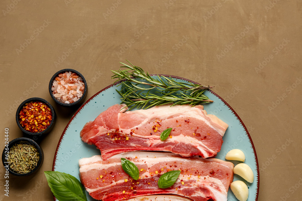 Plate with raw pork ribs, herbs and spices on color background