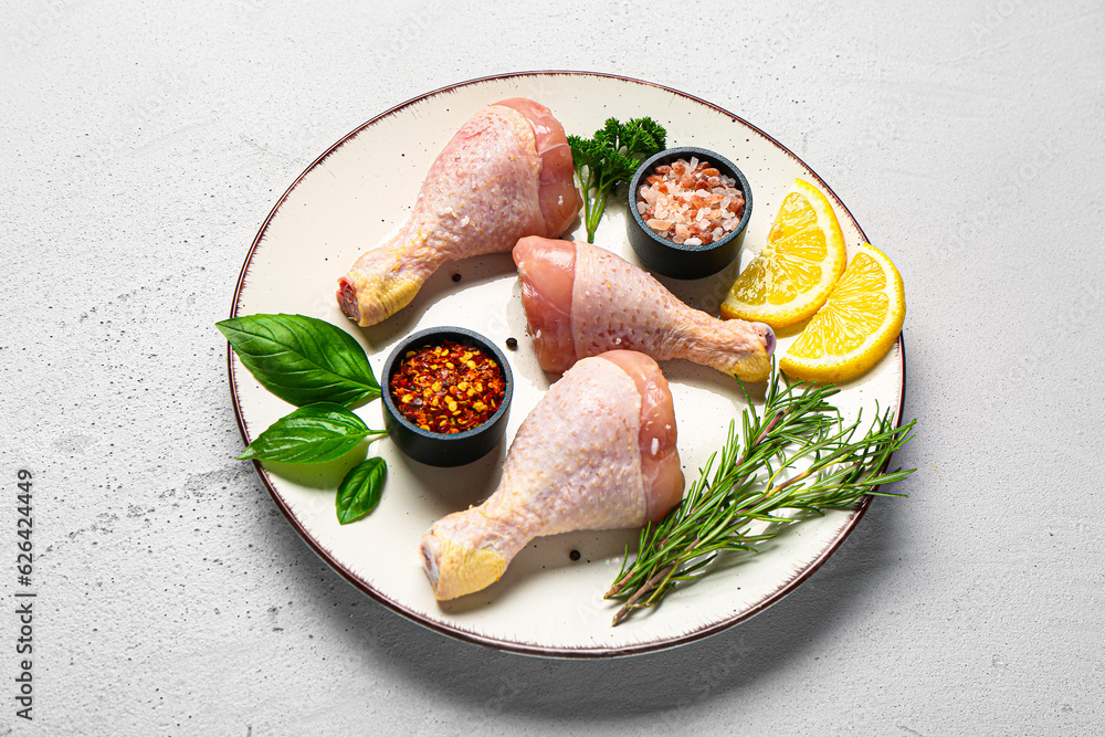 Plate with raw chicken legs, spices and herbs on light background