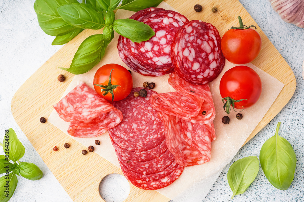 Wooden board with slices of tasty salami on light background