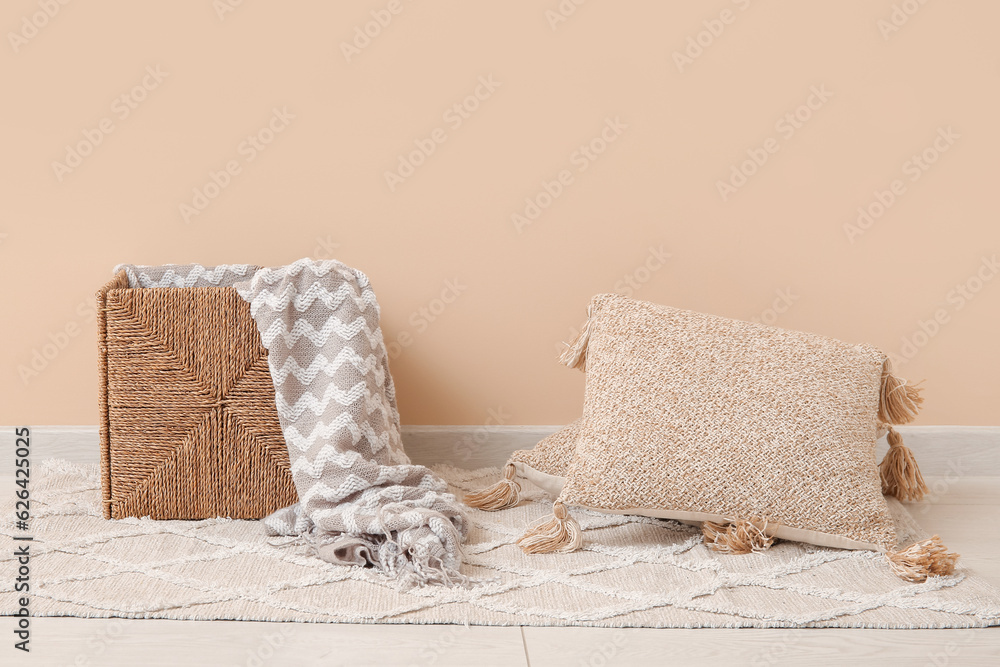 Wicker basket with cozy blanket and cushions near beige wall