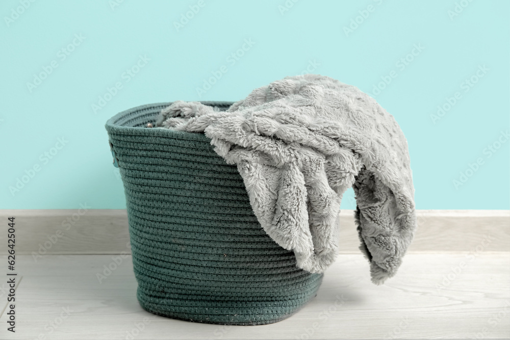 Basket with cozy blanket near blue wall, closeup