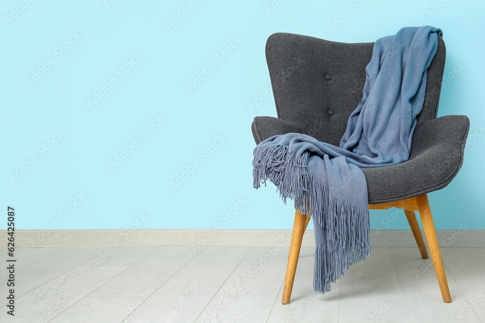 Grey armchair with cozy blanket near blue wall