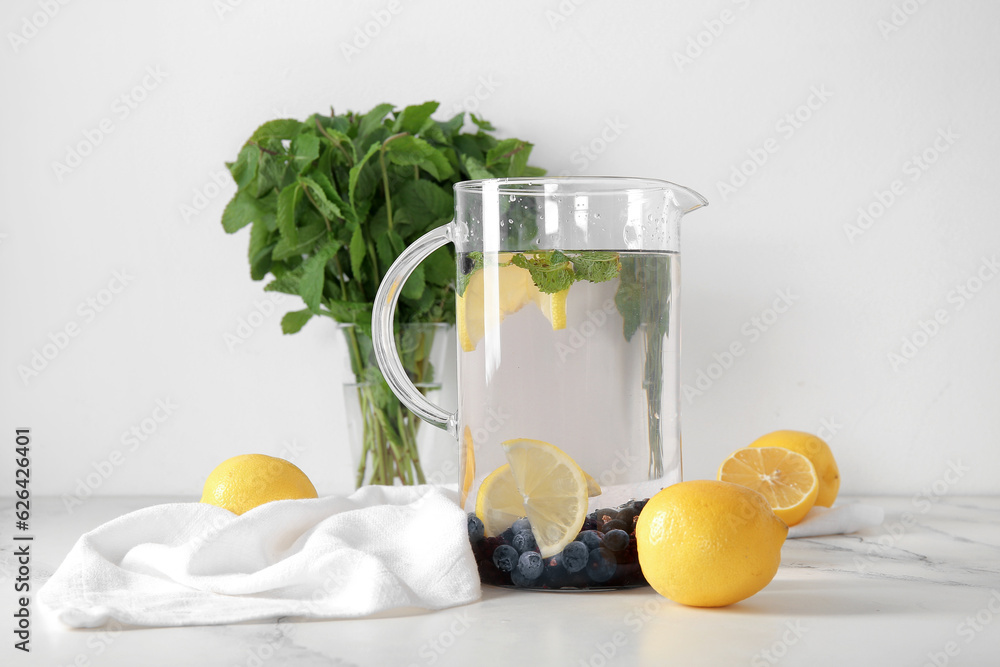 Jug of infused water with blueberries, blackberries and lemon on white background