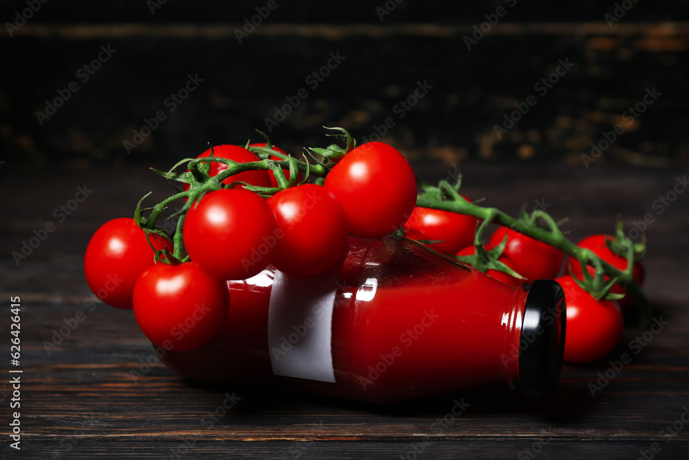 Bottle of tasty tomato juice on black wooden background