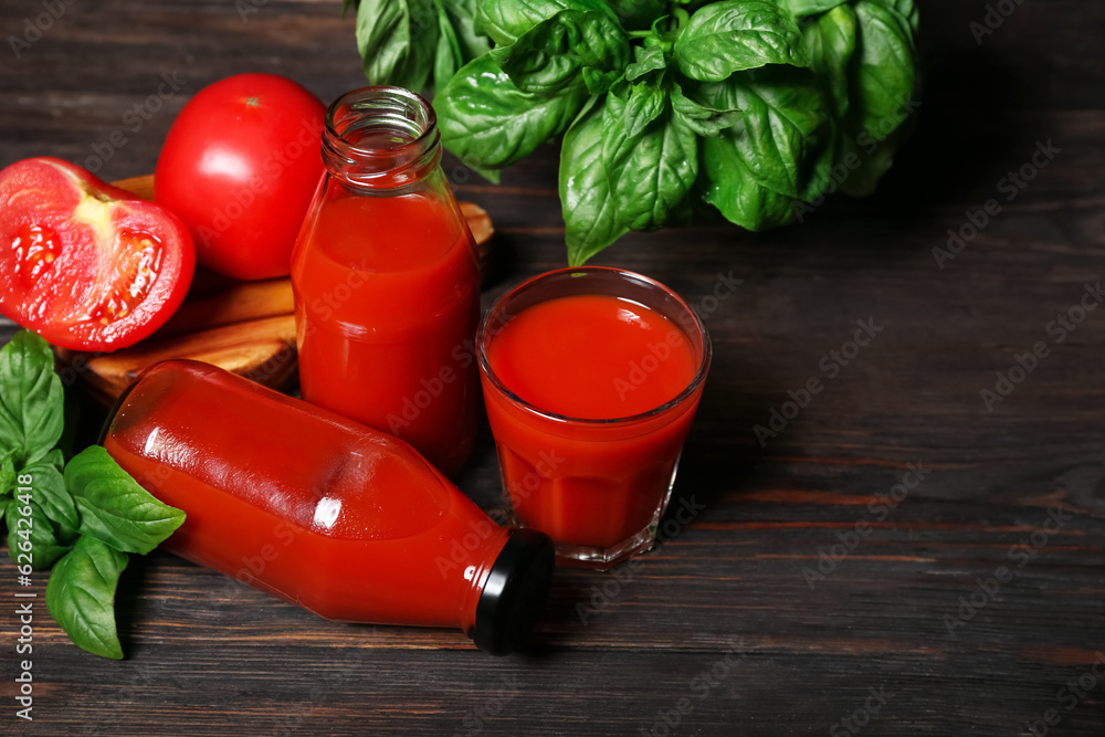 Glass and bottles of tasty tomato juice on black wooden background