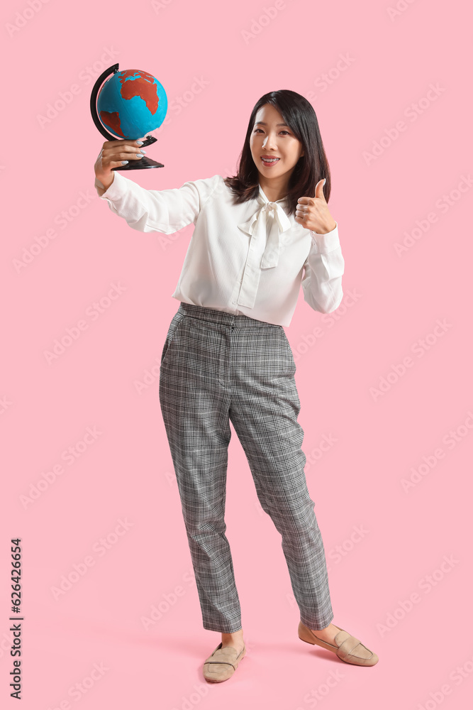 Asian Geography teacher with globe showing thumb-up on pink background