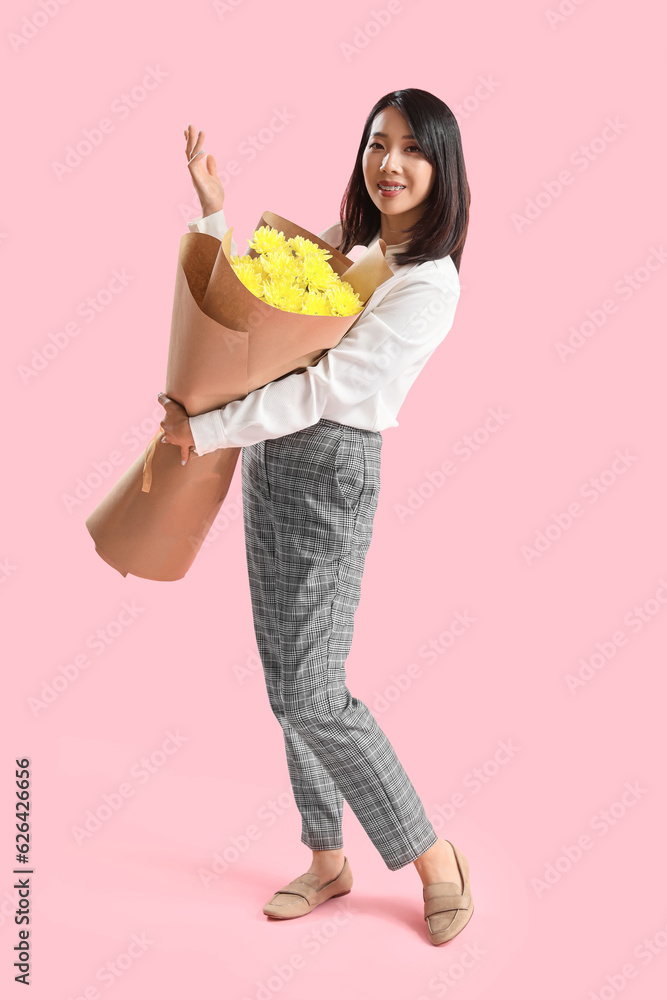 Female Asian teacher with bouquet of flowers on pink background