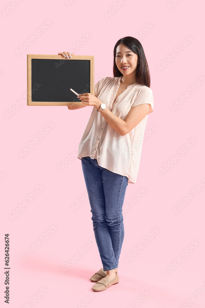 Female Asian teacher with chalkboard on pink background