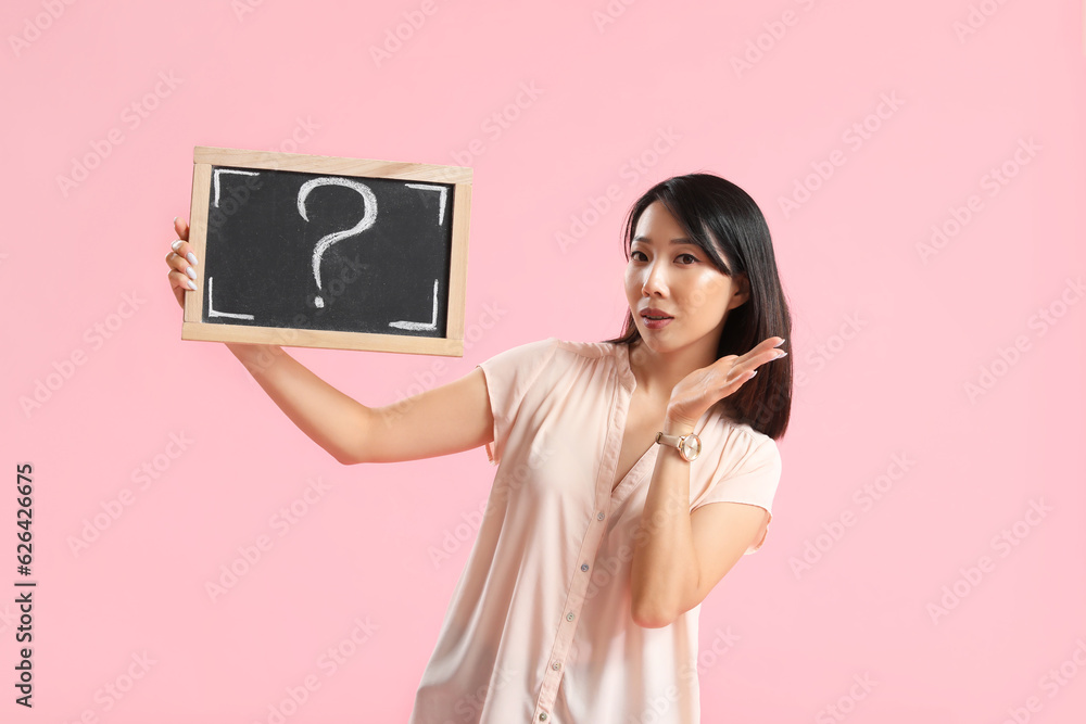 Female Asian teacher holding chalkboard with question mark on pink background