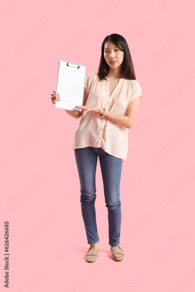 Female Asian teacher with clipboard on pink background