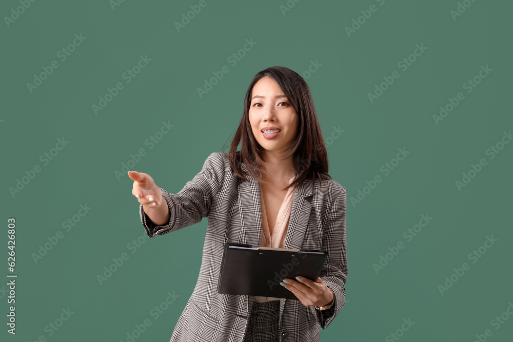 Female Asian teacher with clipboard on green background