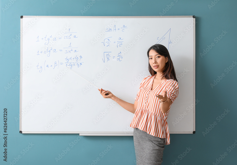 Asian Math teacher with pointer near flipboard in classroom