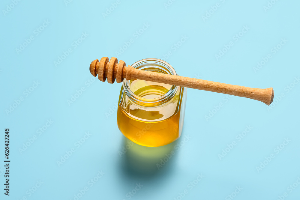 Jar of sweet honey and dipper on blue background