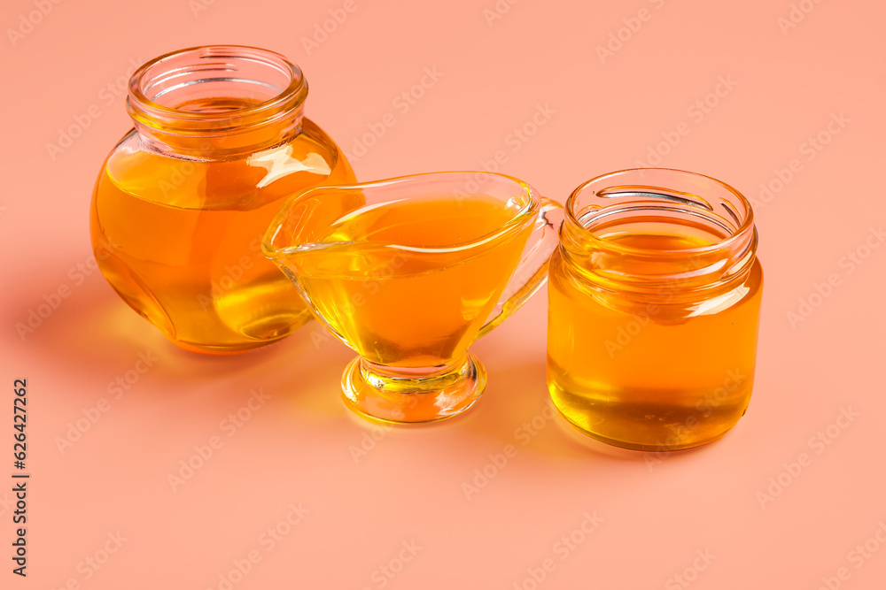 Jars and gravy boat of sweet honey on pink background