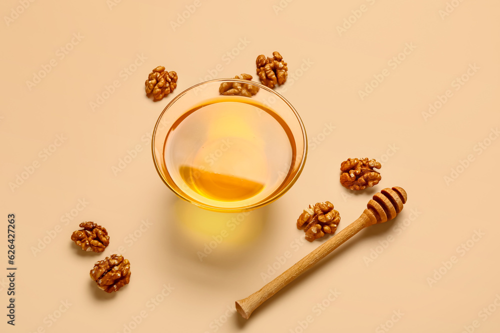 Glass bowl of sweet honey with walnut and dipper on beige background