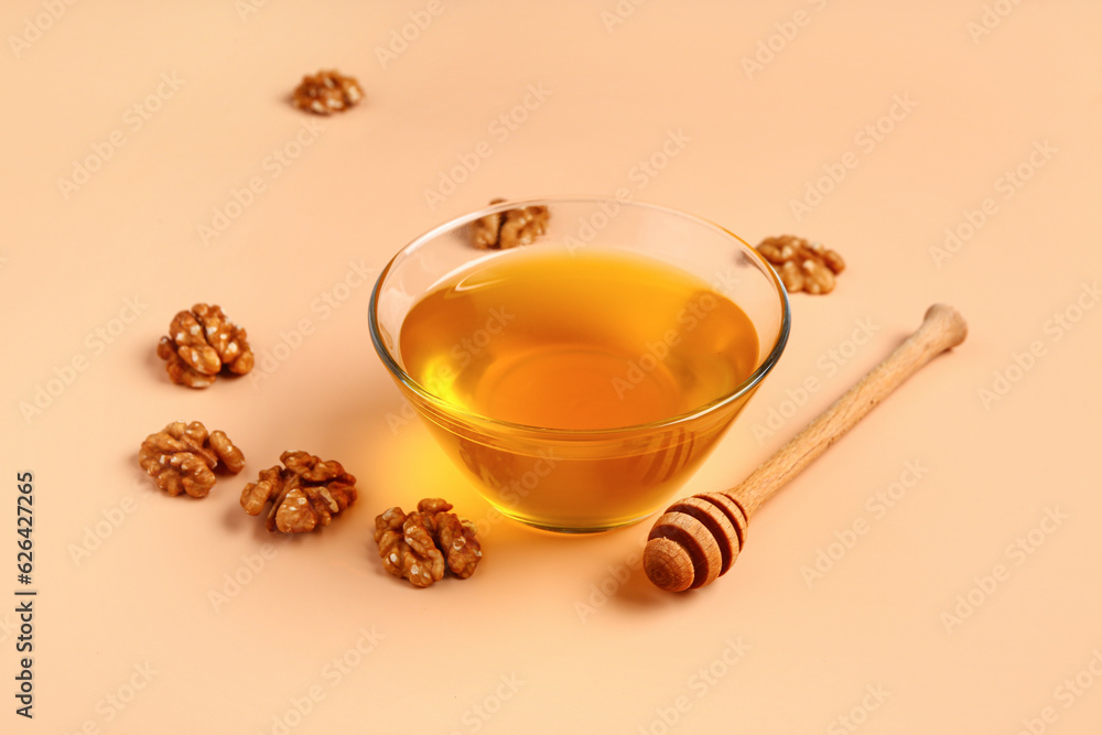 Glass bowl of sweet honey with walnut and dipper on beige background