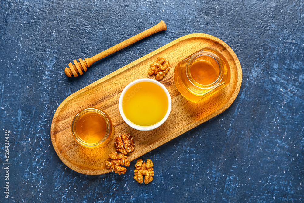 Bowl and jars of sweet honey with walnut on blue background