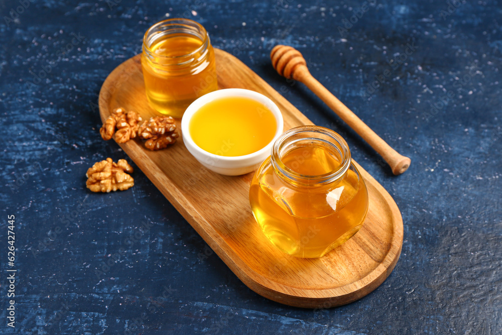 Bowl and jars of sweet honey with walnut on blue background