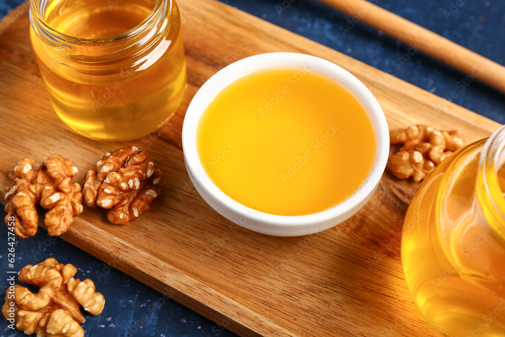 Bowl and jars of sweet honey with walnut on blue background