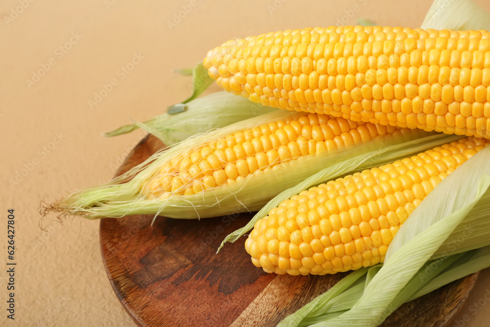 Wooden board with fresh corn cobs on brown background