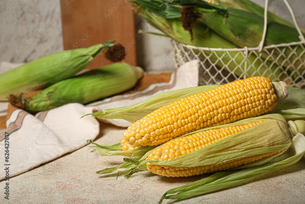 Basket with fresh corn cobs on white table