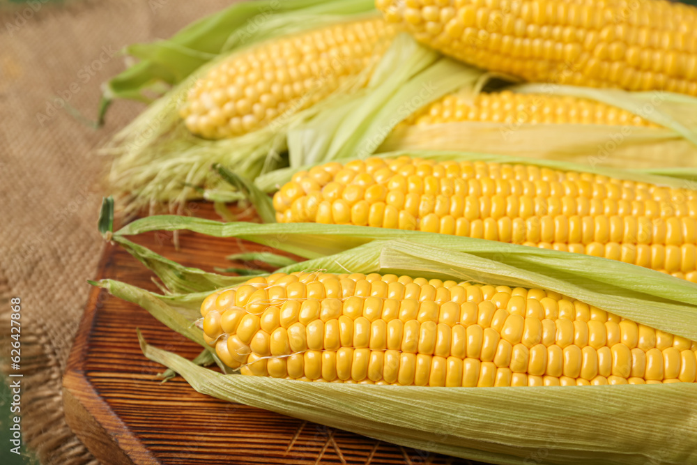 Wooden board with fresh corn cobs, closeup