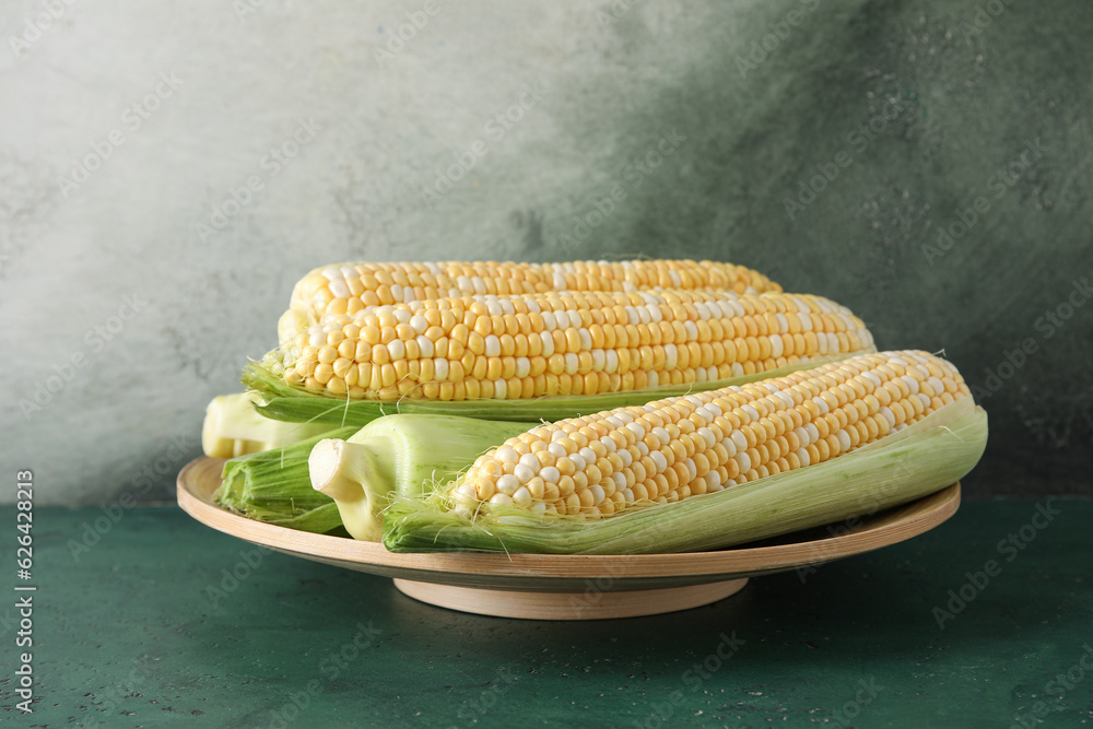 Plate with fresh corn cobs on table